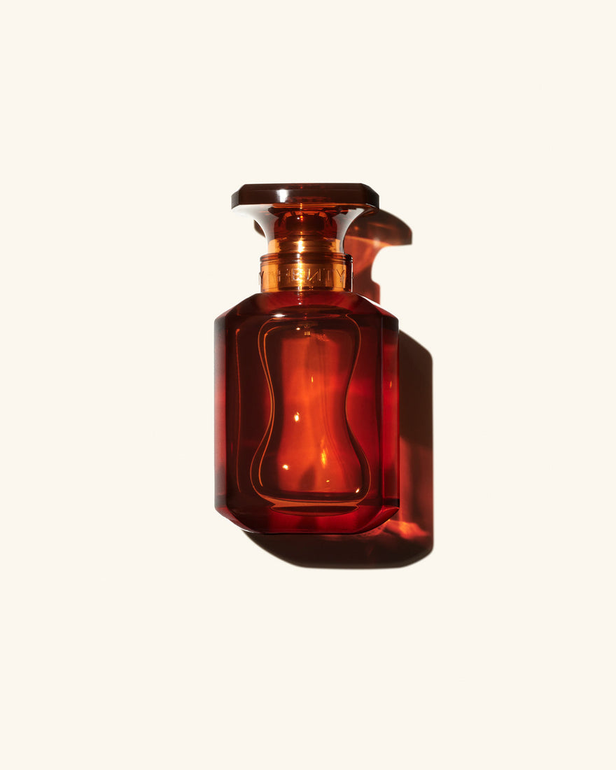 Fenty Eau de Parfum clear chestnut brown tinted glass perfume bottle on beige background